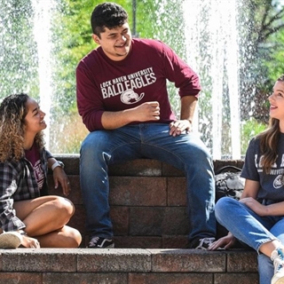 three college students smiling and sitting in front of a fountain