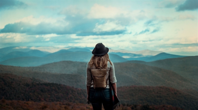 Female hiker with her back to the camera looking out over a blue-tinted mountain range