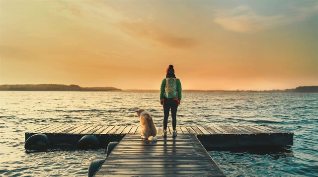 Woman and dog standing on a pier that stretches out into a lake