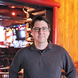 Man standing in front of a log cabin with soft, warm lighting