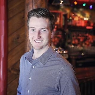 Man standing in front of a log cabin with soft, warm lighting