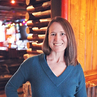 The author in front of a log cabin wall with soft, warm lighting