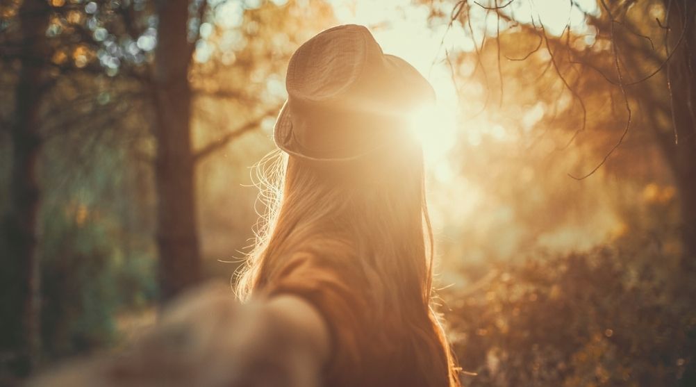 Woman guiding someone through a sunlit forest
