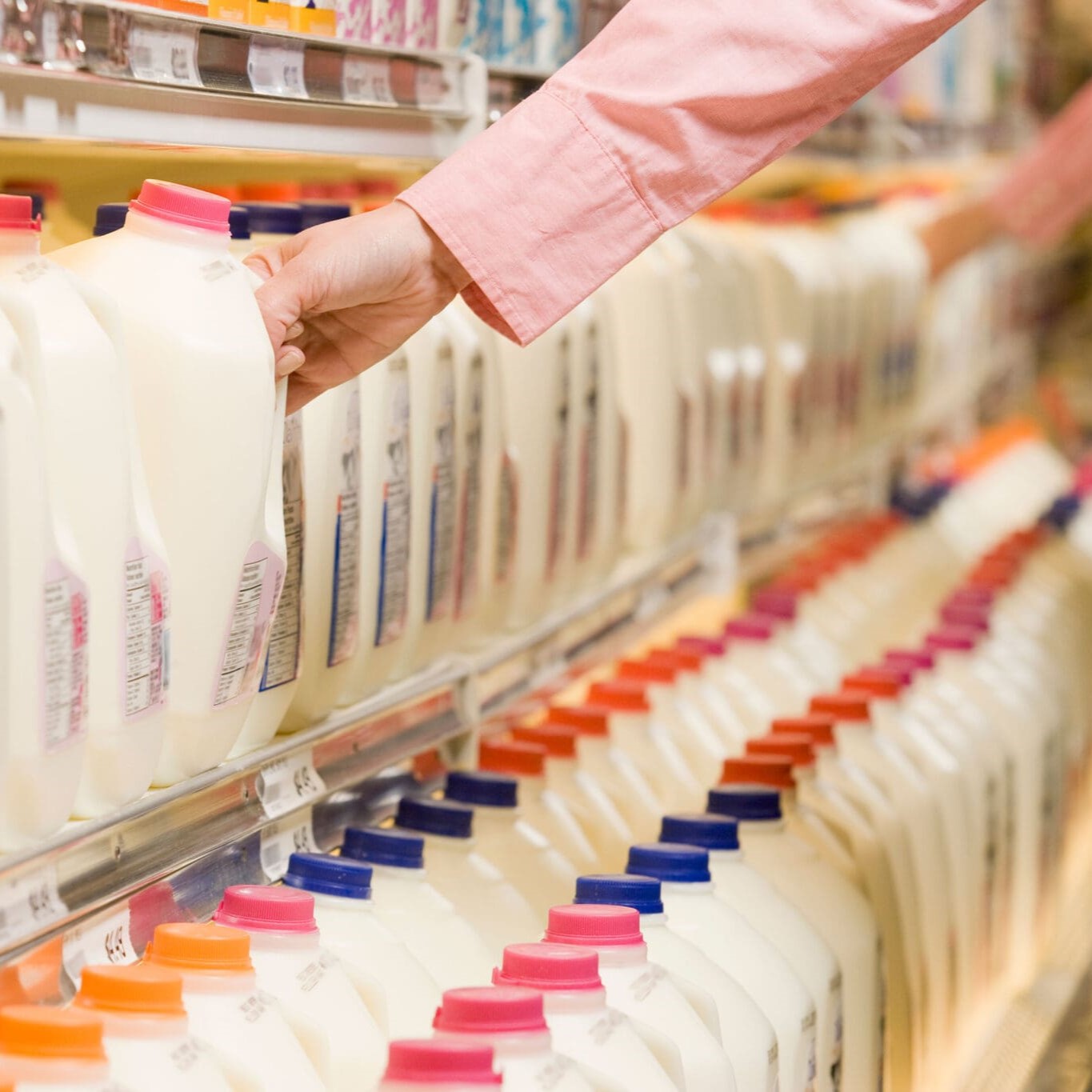 Closeup of a hand reaching for a gallon of milk in a grocery store cooler