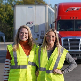 two woman in yellow safety vests standing in front of semi trucks
