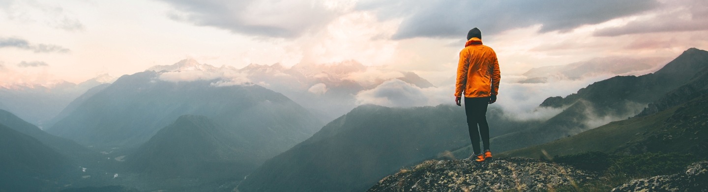 A hiker standing on mountain peak looking out over a mountain range